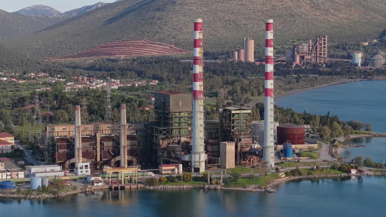 Ripresa orbitale con drone e teleobiettivo che rivela la struttura e le dimensioni della centrale elettrica di Aliveri in Eubea, evidenziandone il design industriale e l'ambiente costiero circostante