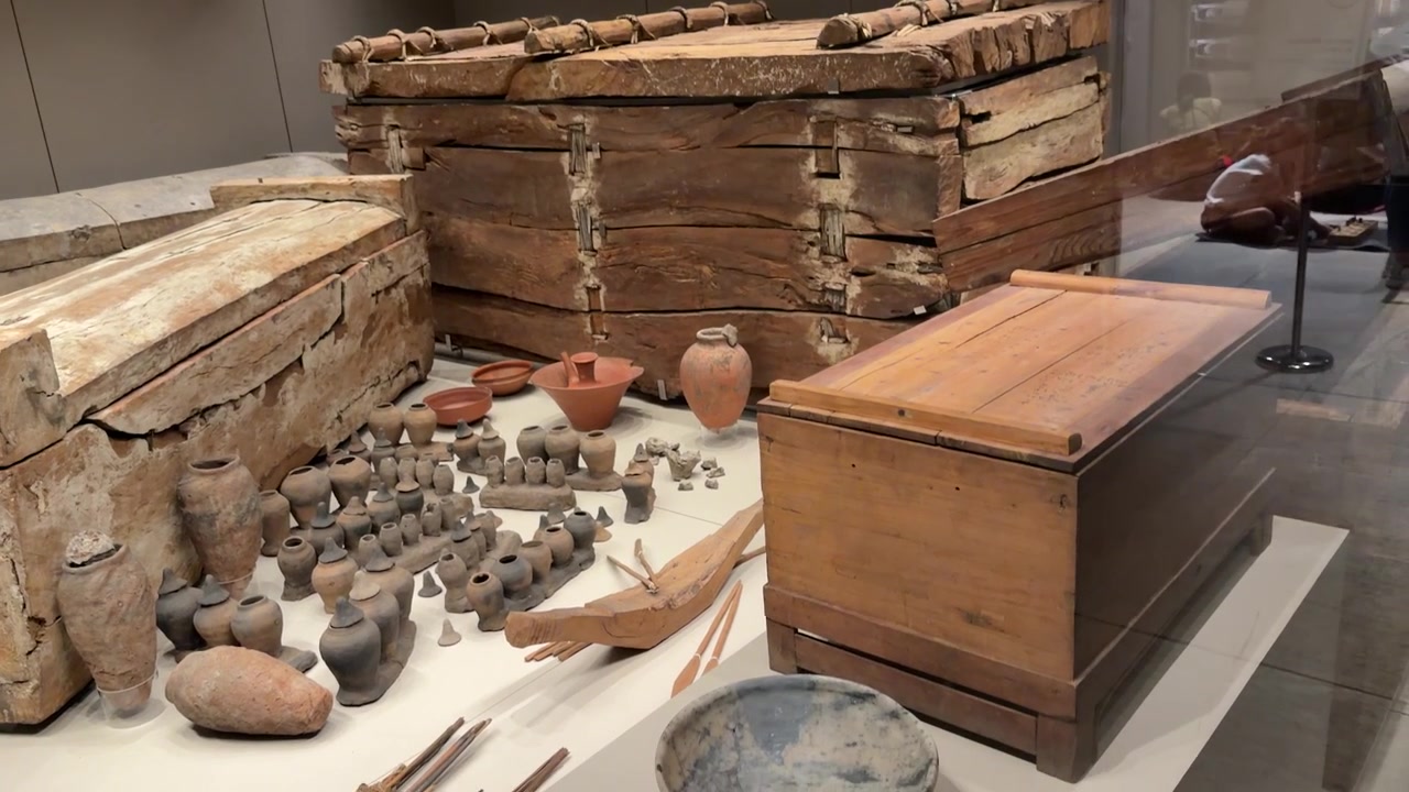 Panoramica di antiche bare di legno e vasellame in terracotta all'interno di uno spazio espositivo museale
