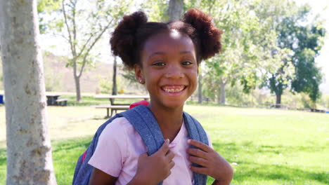 slow motion portrait of young girl with backpack in park smiling at camera