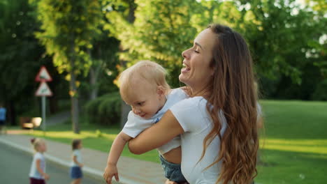 Mother-holding-son-on-hands-outside.-Woman-and-toddler-turning-around-on-street