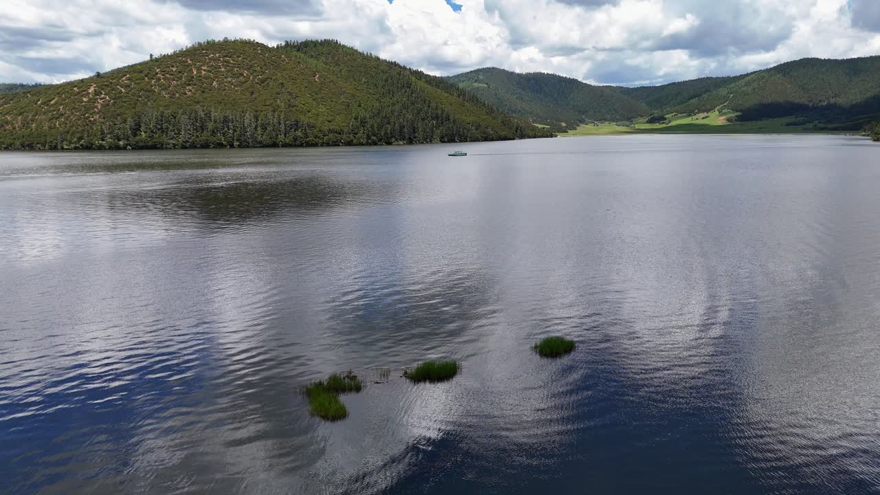Close aerial tracking left of lake surface with ripples and forested mountains in Potatso National Park