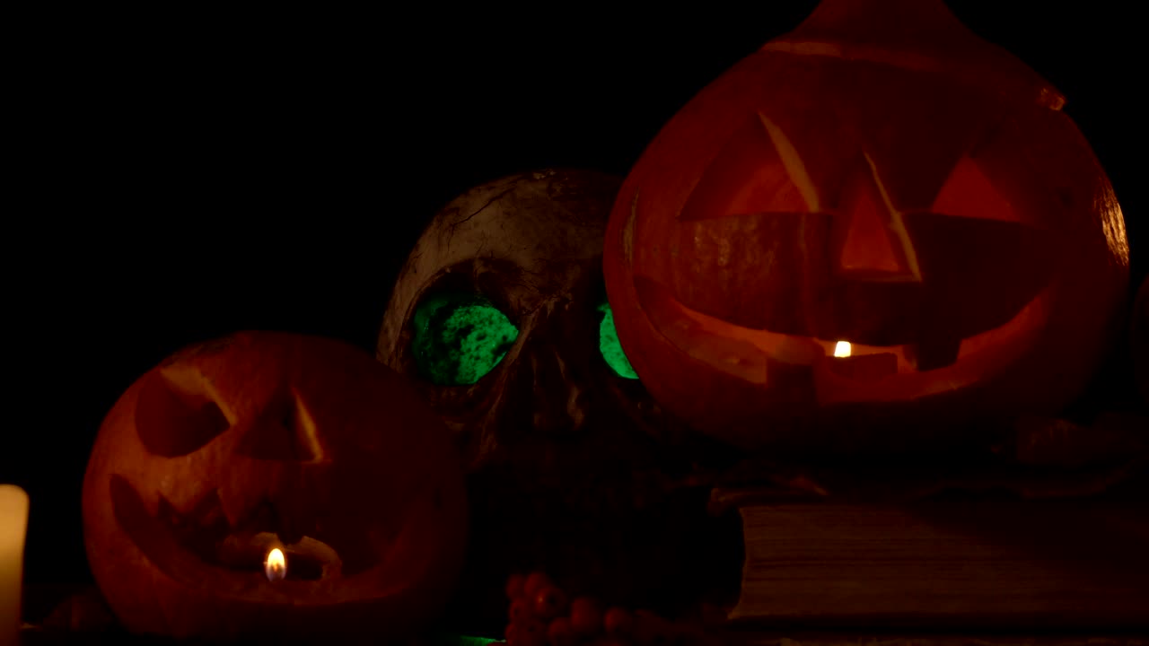 cráneo con ojos brillantes y dos calabazas con velas en el interior, video en bucle