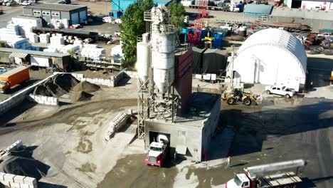 aerial pan left shot of silos on a industrial complex with semi trucks, humans working and heavy equipment moving