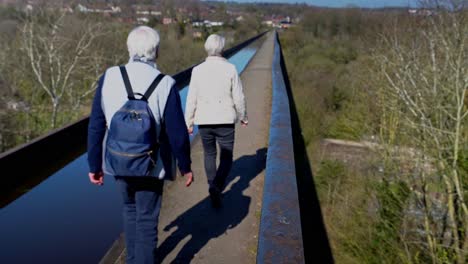 An-elderly-couple-with-grey-hair-walk-across-the-famous-Pontcysyllte-Aqueduct-on-the-Llangollen-canal-route-in-the-beautiful-Welsh-countryside