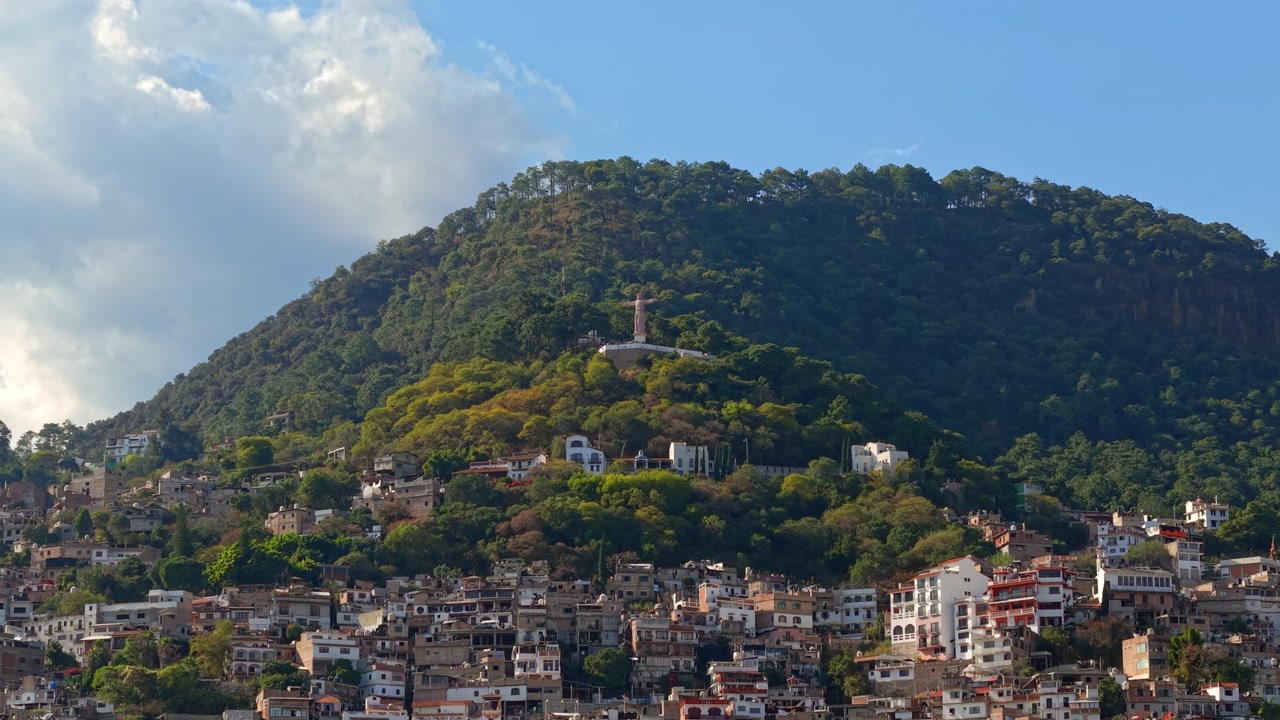 Panoramic aerial view dolly in establishing shot of Atachi Hill with residential houses on its slopes and the monumental Christ statue in Taxco, Guerrero, Mexico