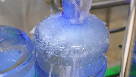 big bottle is quickly filled with fresh water. full bottle is moved by the conveyor line. close up. food factory concept.