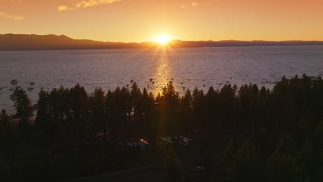dark silhouettes of pine trees on the waterfront of lake tahoe, california, usa. numerous boats sailing on the water. setting sun behind the mountains at backdrop.