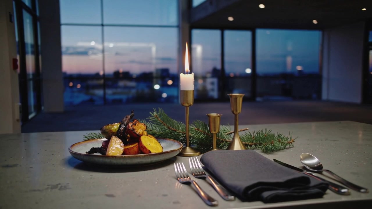 La cámara se aleja revelando una mesa al anochecer, mostrando una vela de latón encendida, plato, servilleta y cubiertos
