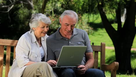 una pareja de ancianos mirando una computadora portátil sentada en un banco