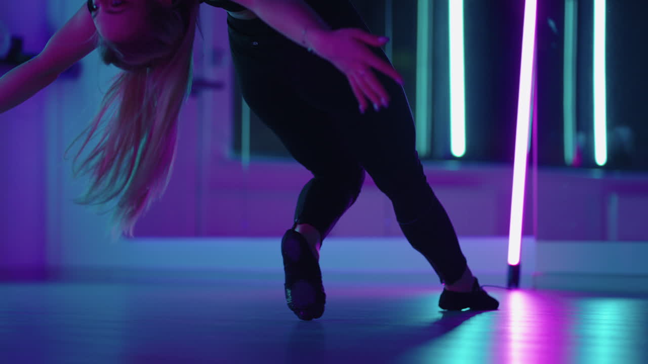 A woman does yoga and stretching on a hanging hammock in neon light. A woman is flying in a hammock in the studio doing stretching and body exercises. Exercises in the air
