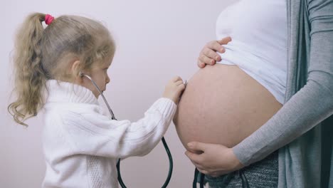 una chica con suéter juega a la doctora con una madre embarazada en la habitación.