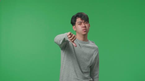 asian man showing thumbs down gesture while standing in front of green screen background