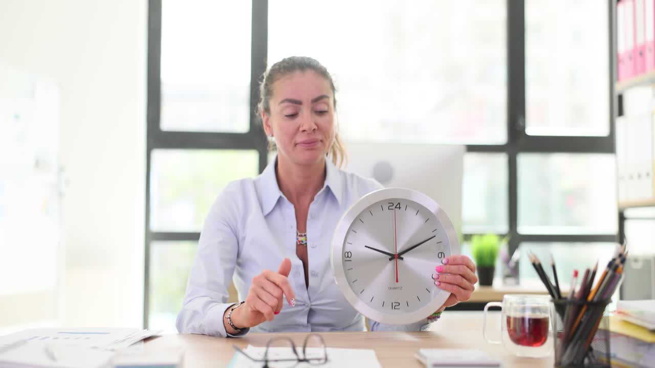 Businesswoman holding and pointing to a clock in an office