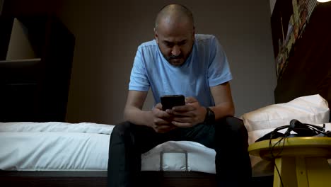 Hombre-De-Viaje-De-Estilo-De-Vida-Sentado-Al-Lado-De-La-Cama-Revisando-El-Teléfono-Inteligente-En-La-Habitación-Del-Hotel