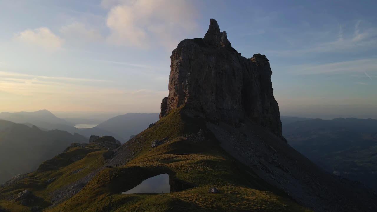 Aerial dolly over lush green meadow and pond of Gross Achslenstock, Schwyz, Switzerland, surrounded by dramatic cliffs and mountain peaks