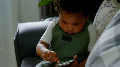 front view of cute little black boy sitting on couch and using mobile phone in a comfortable home 4k