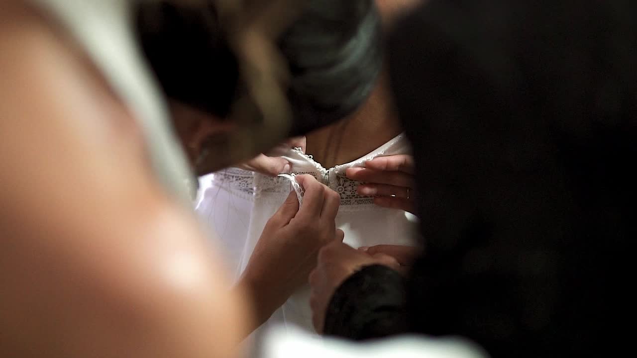 Woman buttoning a bride's dress on her wedding day