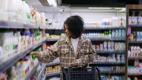 Positive-black-woman-with-mobile-device-and-trolley-purchasing-products-at-mall