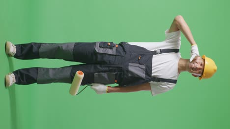 full body of asian man painter wearing safety helmet smiling and making call me gesture to camera while standing in the green screen background studio