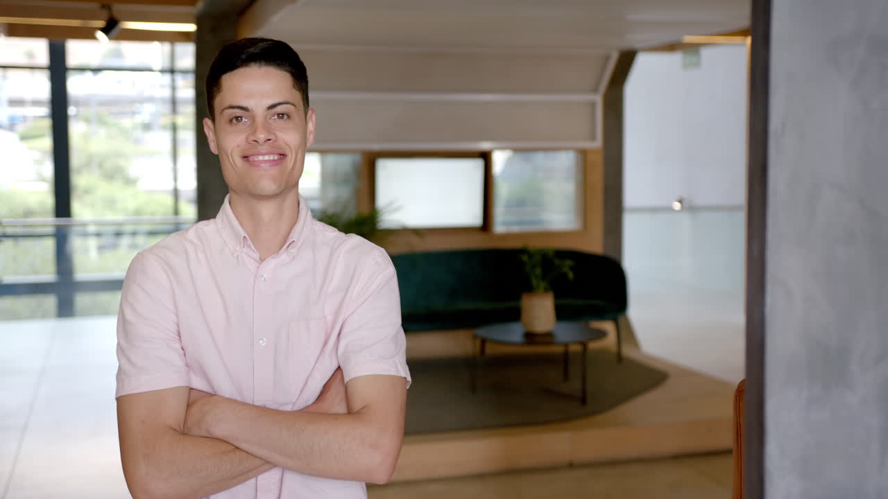 Smiling man standing with arms crossed in modern office lobby, copy space