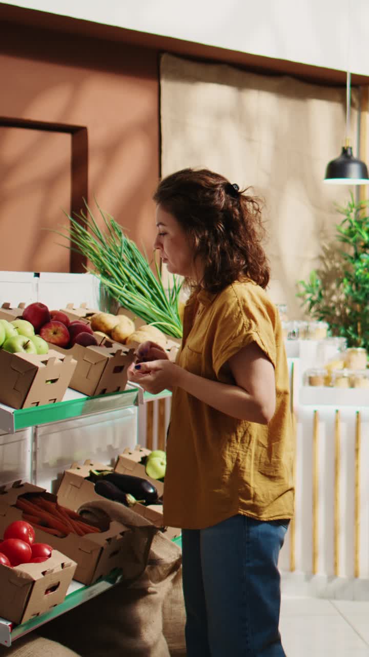 Vídeo vertical. Una mujer comprueba si las manzanas de una tienda bio son ecológicas