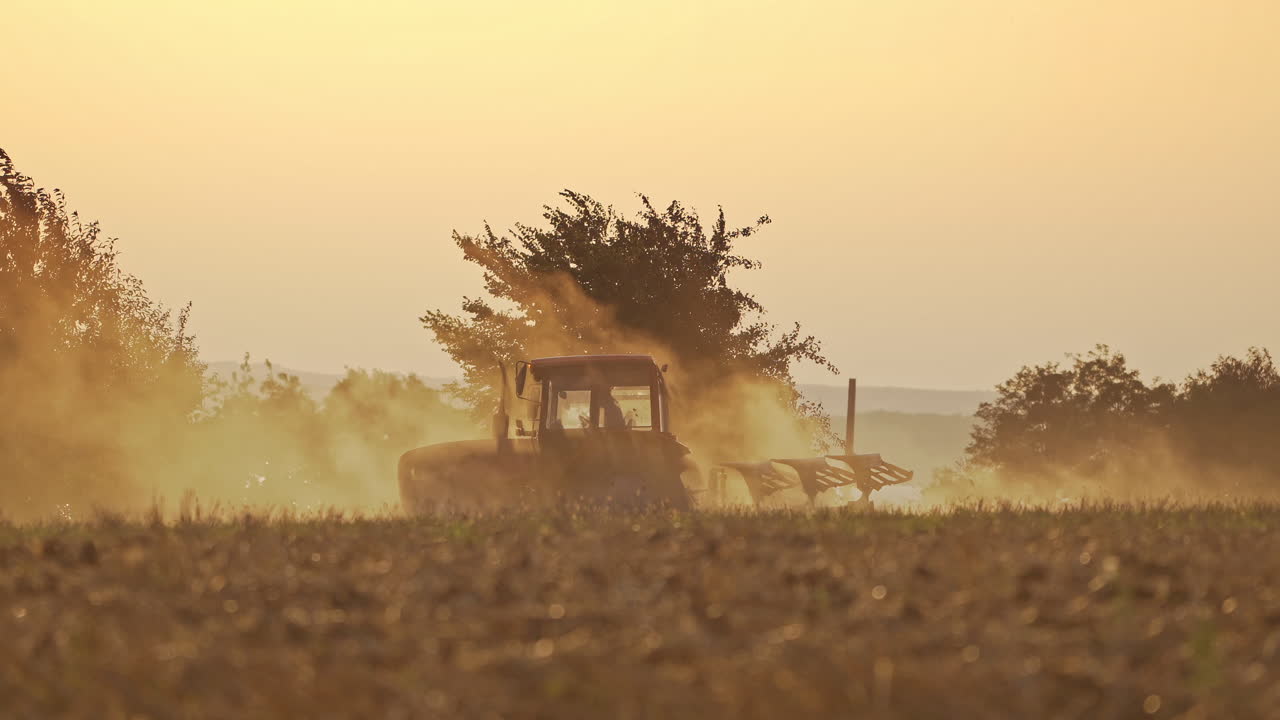 Agricultural machine cultivates the soil on natural dust background. Tractor working on the field in the morning outdoors.