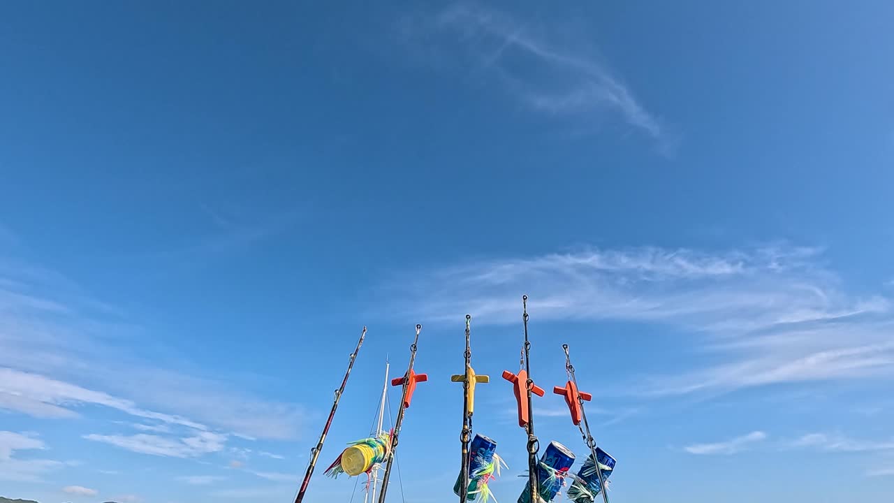 Fishing rods with colorful lures sway gently on a boat in Phuket, Thailand, under clear blue skies