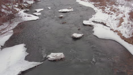 top view of a almost frozen river in winter time near a deciduous forest in romania