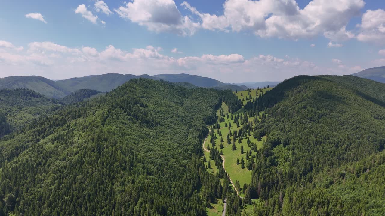 Aerial view gliding forward across the Low Tatras, capturing a broad mountain valley framed by deep green forests and gently sloping hills on a warm, clear summer day