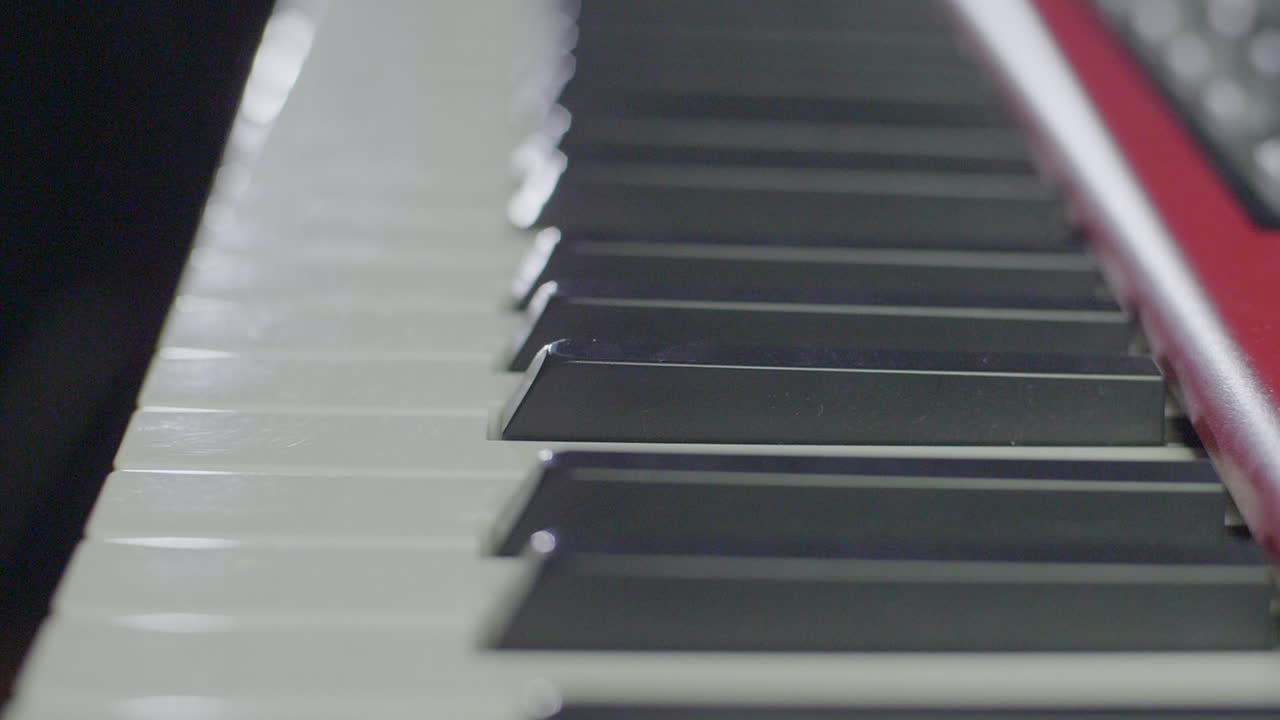 Slow motion close up of an electric stage piano synthesizer keyboards keys in front of a dark background with led stage light scenery. Backwards gimbal camera movement. Shot in 4K at 120fps.