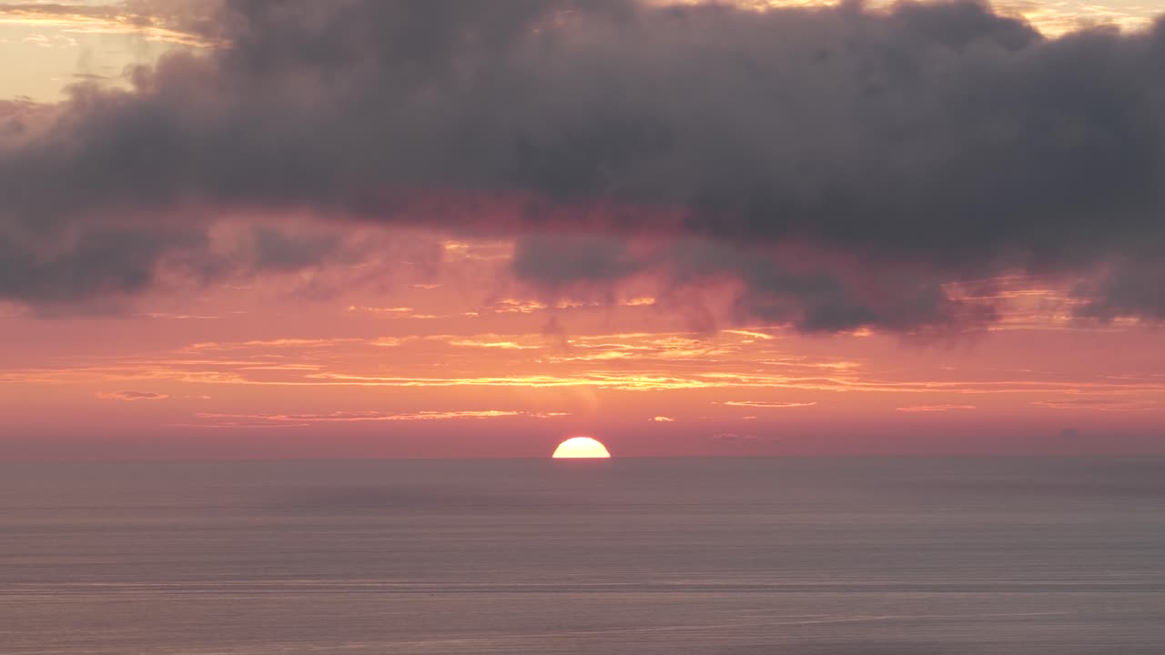 色とりどりの雲が浮かぶ海の地平線に沈む鮮やかな夕焼け