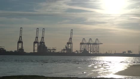 tide slow moving on shimmering sunset golden river water with british harbour port cranes silhouettes skyline