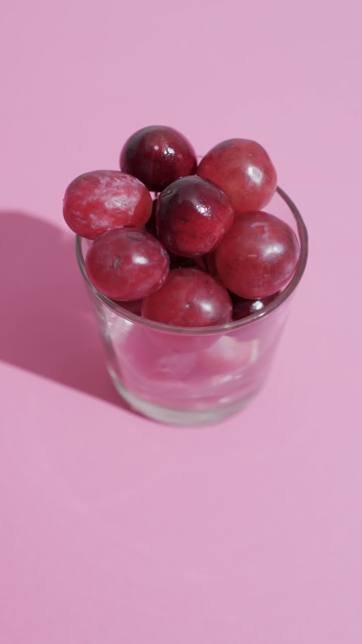 Vertical video of red grapes in glass with copy space on pink background