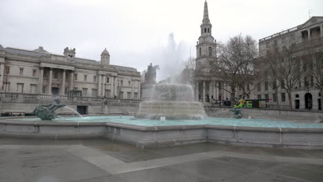 slow motion shot of one of the trafalgar square's fountains, the king george statue and a ambulance passing by