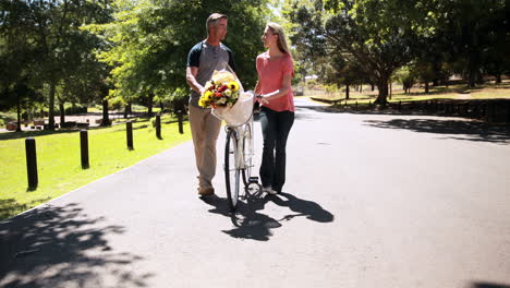 Pareja-Feliz-Caminando-Con-Bicicleta-Y-Ramo-De-Flores