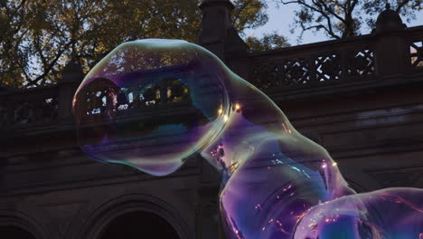 big giant soap bubble shape floating in air, dragged by breeze, moving expanding and bursting, colorful transparent shape blast burst outside in park