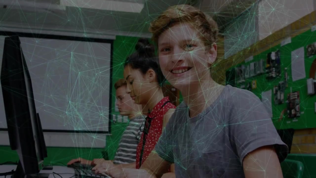 Camera panning upward revealing three students coding at keyboards and pausing and smiling in lab