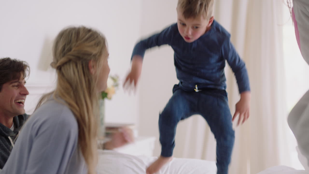 happy family with children jumping on bed playing with mother and father having fun on weekend morning excited little kids enjoying game with parents at home 4k footage