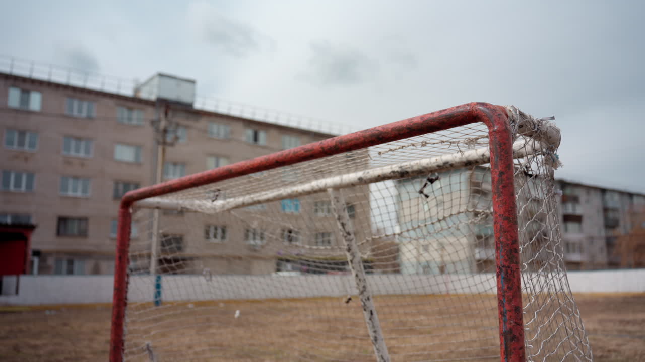 Заброшенная спортивная площадка с коррозией, обветшалое спортивное поле с проржавевшими футбольными воротами и унылой атмосферой, заброшенная зона отдыха с полуразрушенными воротами под мрачным серым небом