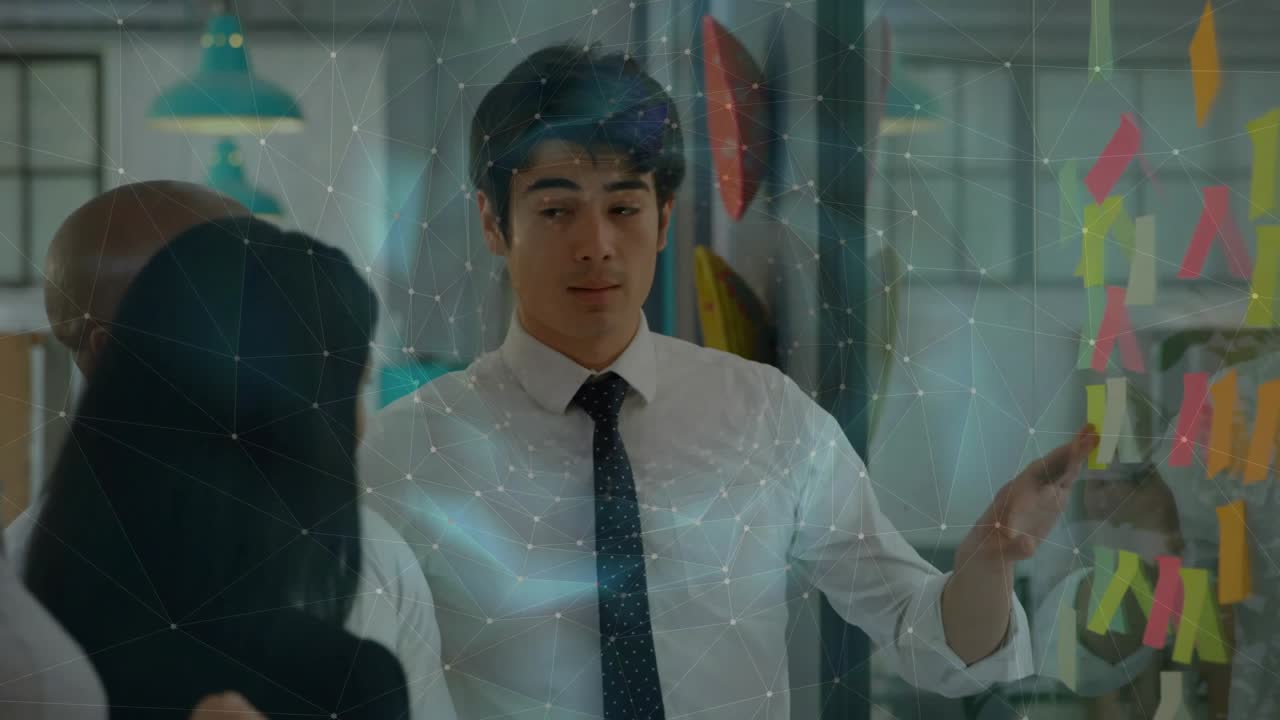 Business team gathering sparking man wearing tie laying out ideas using sticky notes on glass board