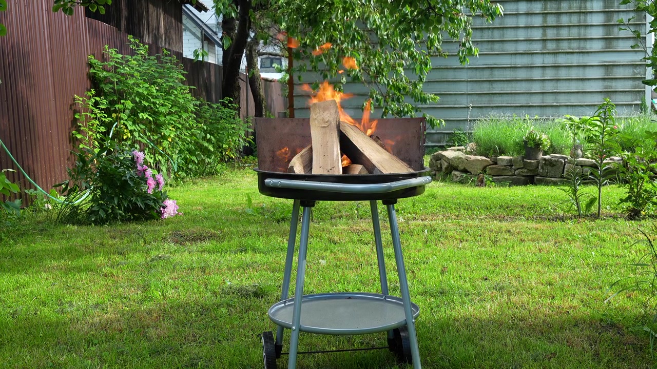 Filmato al rallentatore di fiamme che bruciano su una griglia per barbecue a carbone in un tranquillo giardino sul retro