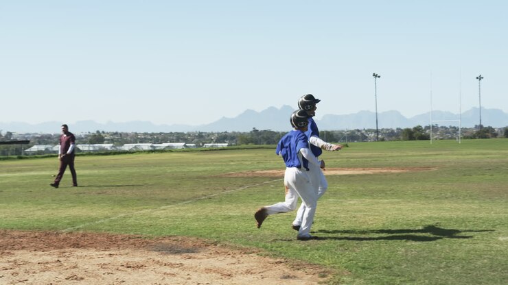 Giocatori di baseball multietnici che corrono, festeggiano e si abbracciano su un campo da gioco, al rallentatore.