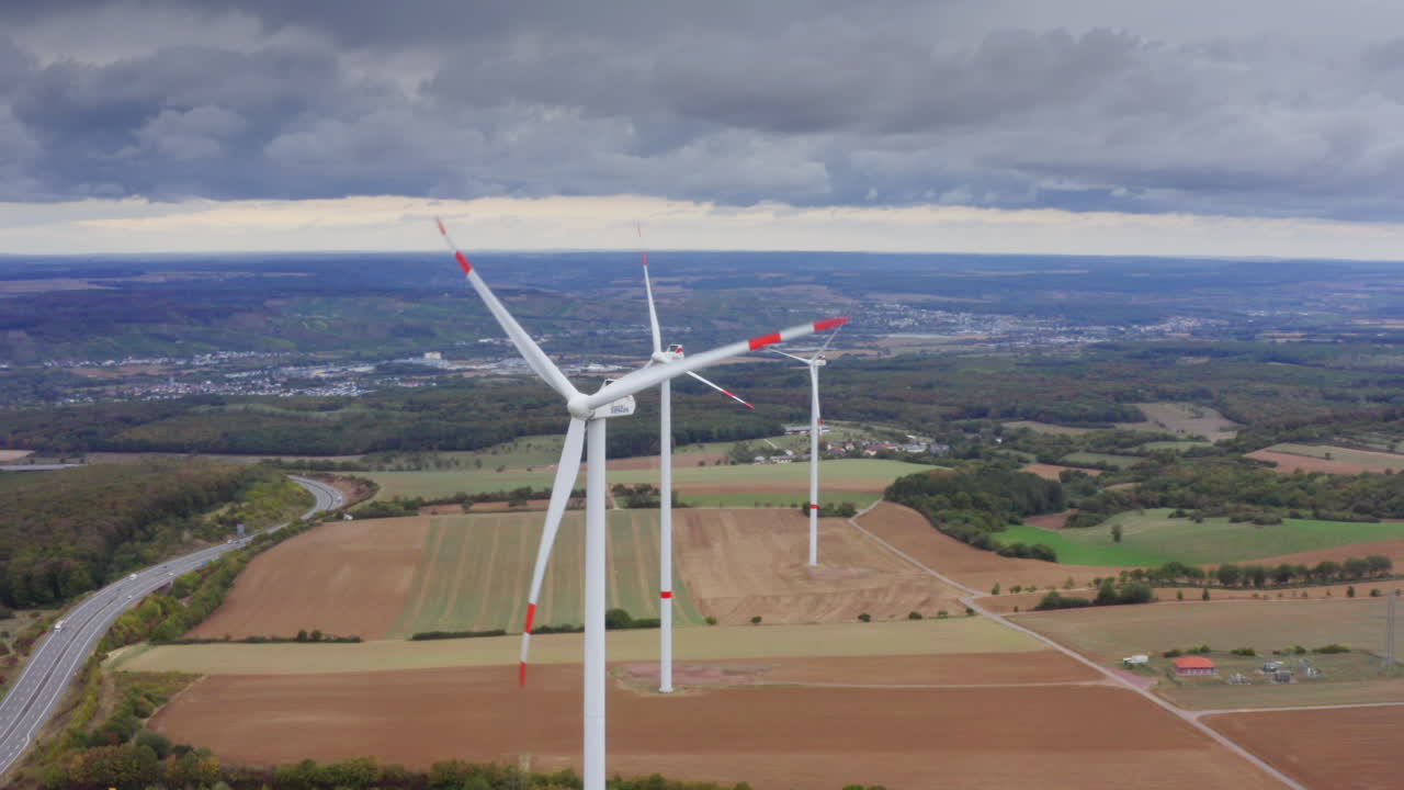 High Quality aerial view of wide fields with tall wind turbines above autumn trees calm sky renewable energy landscape in Luxembourg clean light soft colors and a peaceful cinematic atmosphere
