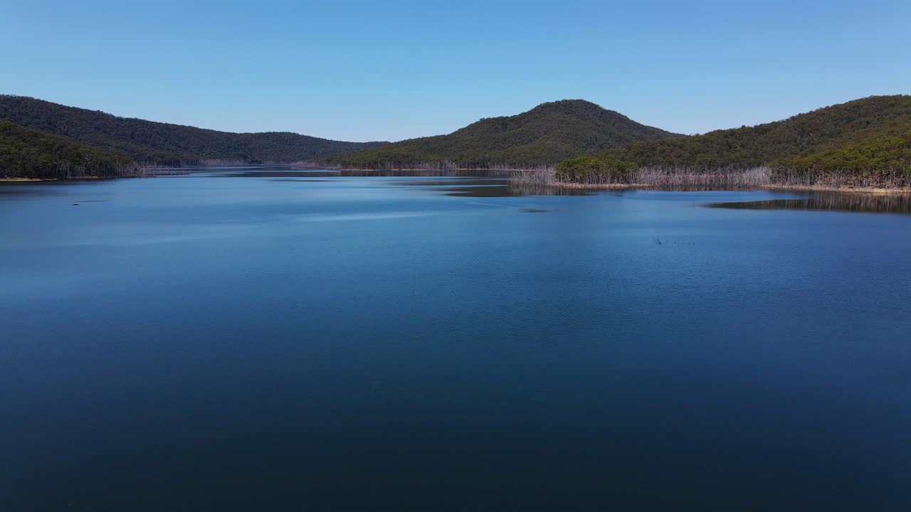todavía agua azul del lago advancetown con montaña boscosa en el fondo - represa hinze - costa dorada, qld, australia