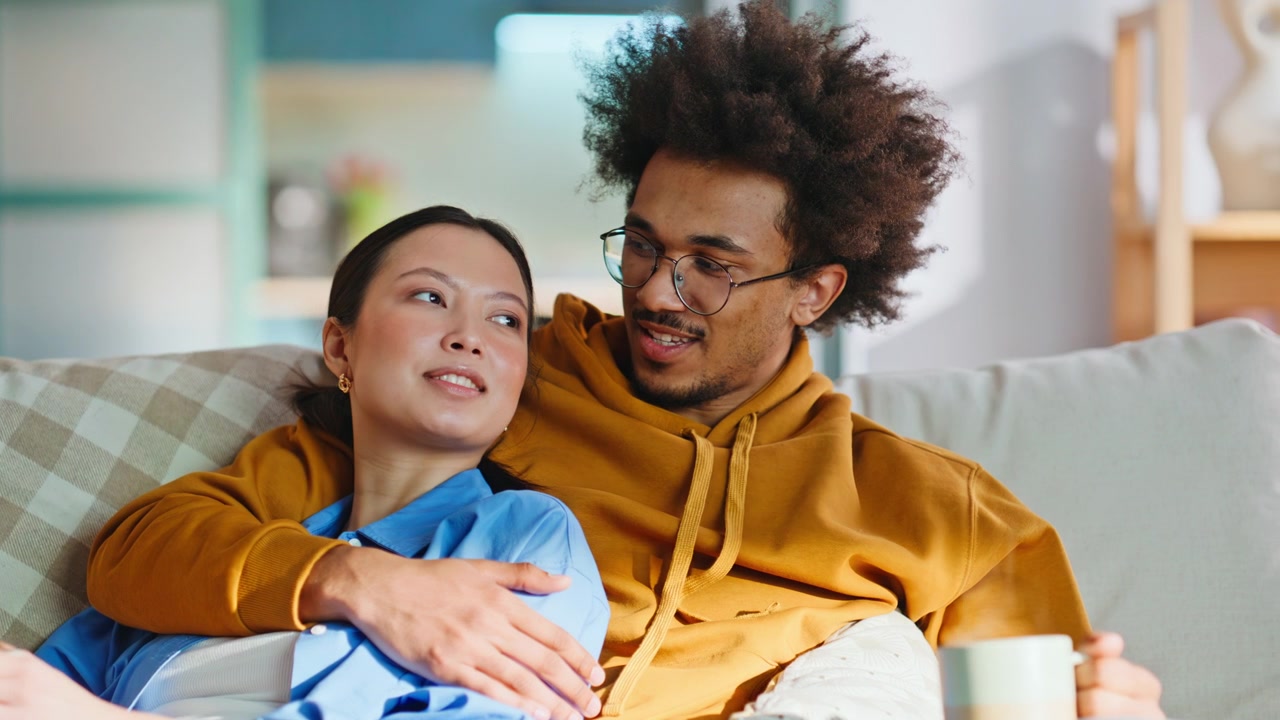 Young couple relaxing on sofa watching TV together. Close up weekend morning.