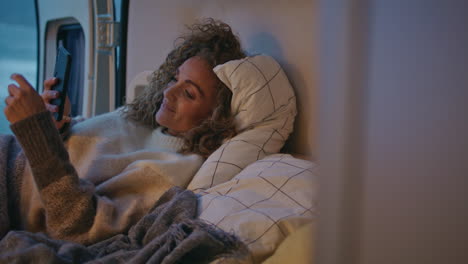 mujer enviando mensajes de texto a un teléfono inteligente acostada en el tráiler de la cama de primer plano. mujer madura sonriente navegando