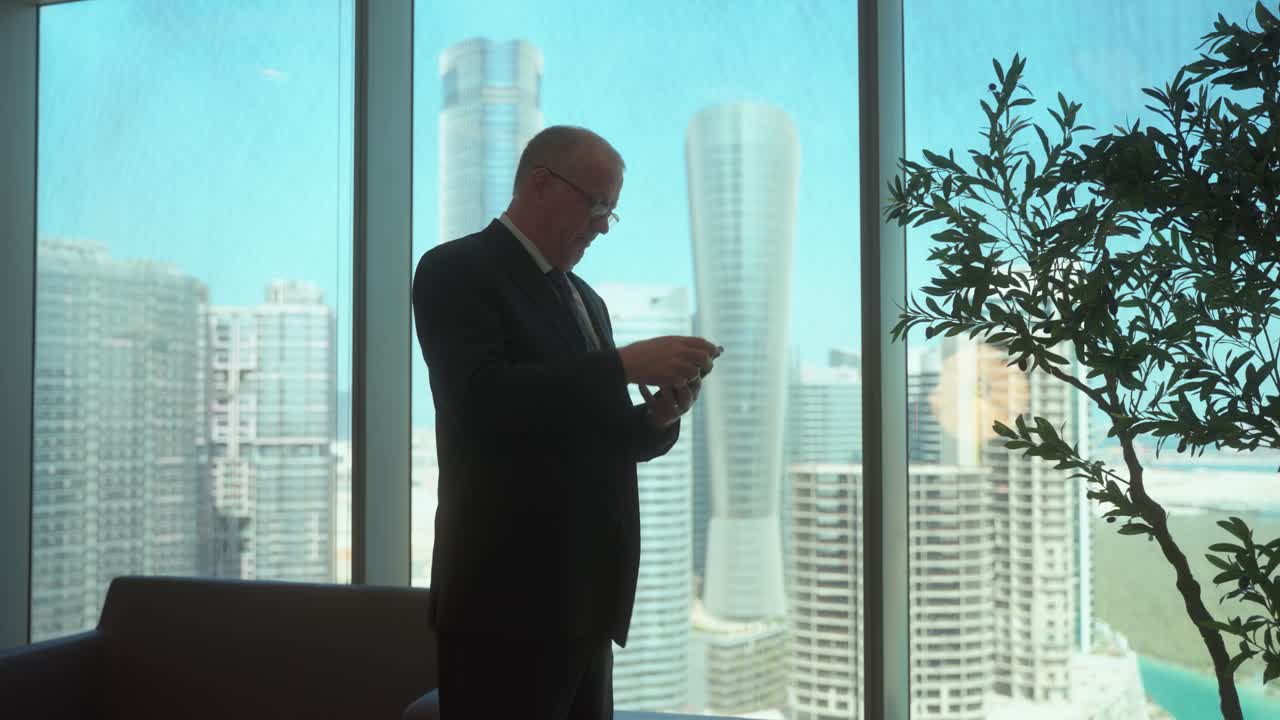 Executive in a skyscraper office checks his smartphone and is receives good news on his smartphone