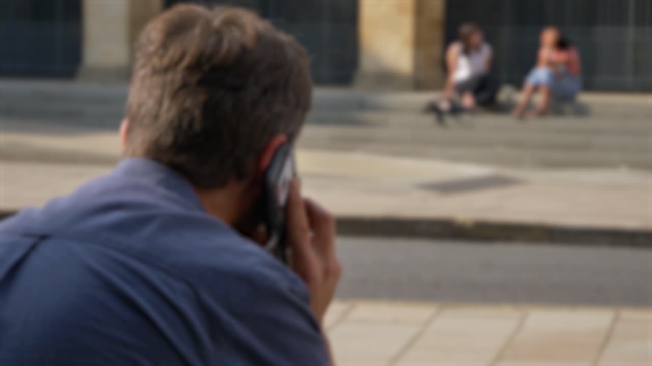 Scatto sfocato di un uomo che parla al telefono seduto per strada a Oxford 01