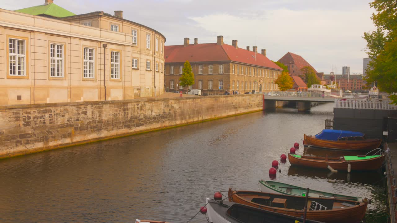 A classic scene of the Danish capital, featuring a calm canal lined with historic, centuries-old buildings and a collection of traditional wooden boats