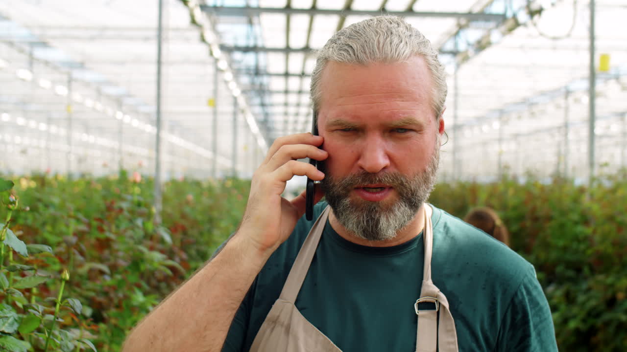 Midaldrende mand går i blomsterdrivhus og taler i telefon